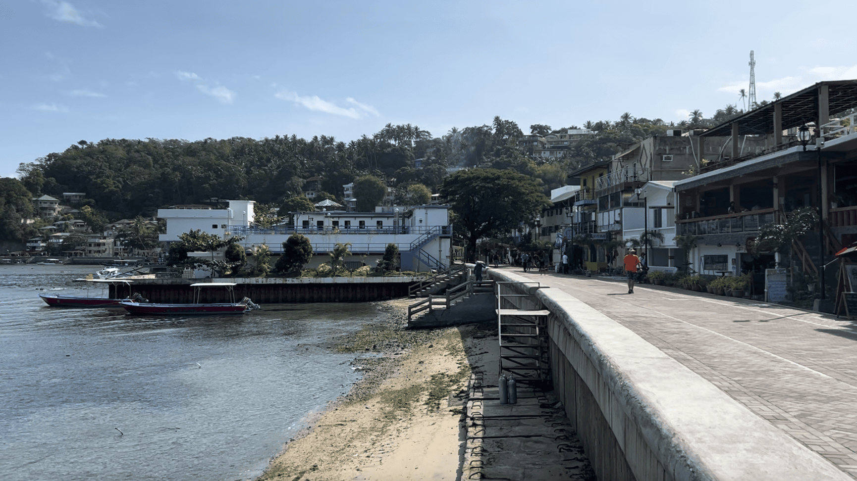 morning view of the Sabang Beach boardwalk in Puerto Galera with boats docked by the shore and hillside buildings in the background